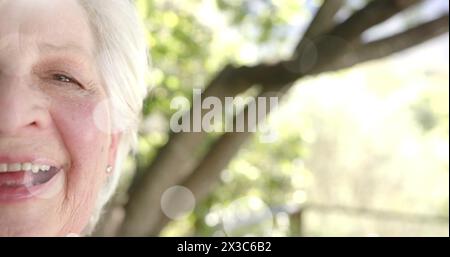 Immagine di macchie di luce e alberi sopra una donna caucasica sorridente in giardino Foto Stock