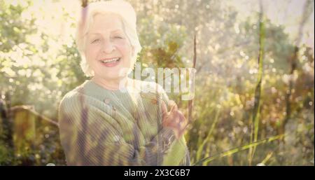 Immagine di macchie di luce e alberi sopra una donna caucasica sorridente in giardino Foto Stock