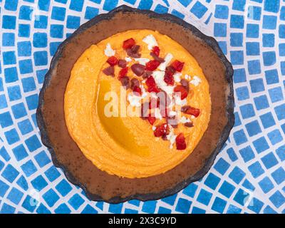 Htipiti, un antipasto greco a base di feta e peperoni rossi arrostiti, in una ciotola di ceramica, su un tavolo a mosaico blu e bianco, vista dall'alto, piano Foto Stock