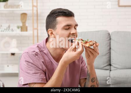 Giovane che mangia un pezzo di gustosa pizza a casa Foto Stock