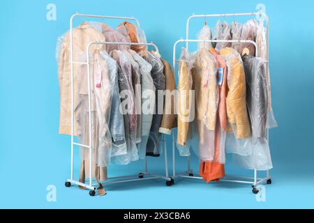 Rack con vestiti in sacchetti di plastica dopo il detergente a secco su sfondo blu Foto Stock