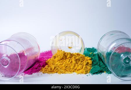 Rosa, verde, giallo tre diversi colori di polvere holi e vasetti di vetro su sfondo bianco. Holi Festival Foto Stock