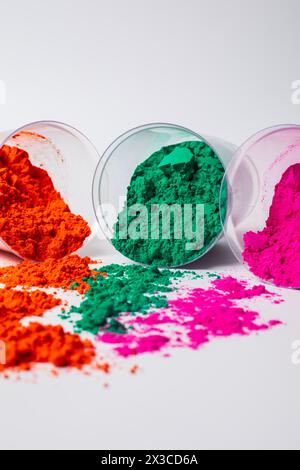 Tre vaschette di vetro appoggiate su uno sfondo bianco con polveri di holi multicolore sparse da esso. Messa a fuoco selettiva Foto Stock