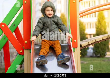 Un bambino sorridente di tre anni cavalca su un'altalena in un parco giochi. Intrattenimento per bambini. Infanzia e infanzia Foto Stock