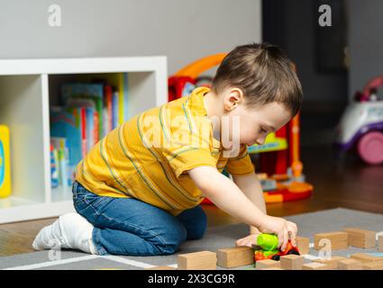 Il bambino con una bendatura o un gesso sulla gamba gioca con giocattoli e blocchi. Frattura di un piede e di un dito nei bambini. Salute umana e medicina con Foto Stock