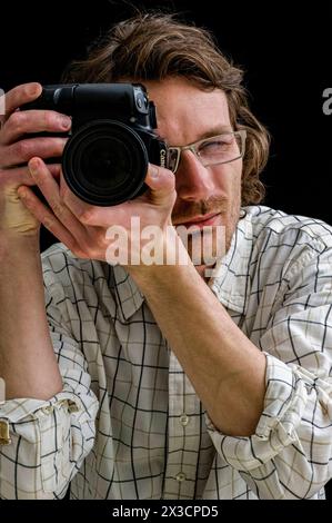 Ritratto uomo con fotocamera Ritratto di un giovane adulto, uomo caucasico che utilizza una fotocamera digitale mentre indossa gli occhiali. Tilburg, Paesi Bassi. MRYES Tilburg Studio Tuinstraat Noord-Brabant Nederland Copyright: XGuidoxKoppesx Foto Stock