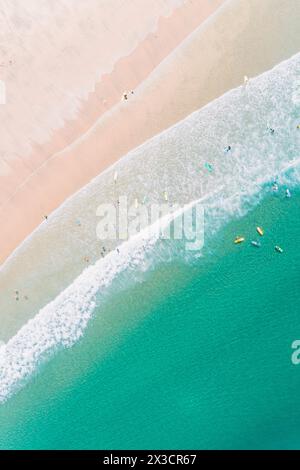 vista aerea zenithal di una spiaggia con acqua turchese, con persone sulla riva di una spiaggia che si godono l'estate e imparano a fare surf. Foto Stock