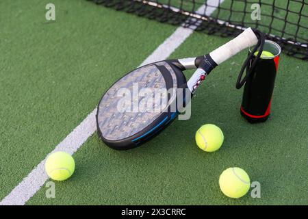 Racchetta da padel blu e palle gialle posizionate sul campo vicino alla rete nelle giornate di sole Foto Stock