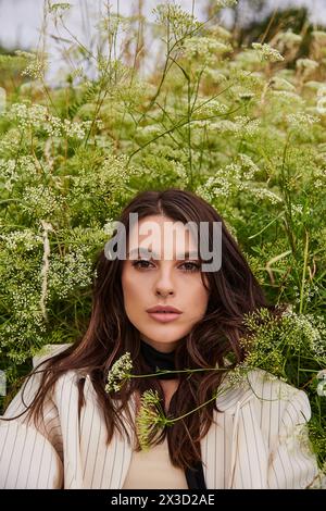 Una bella giovane donna in abito bianco si erge graziosamente in un campo di erba alta, abbracciando la dolce brezza estiva. Foto Stock