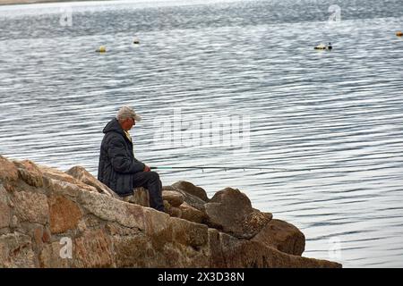 Bouzas, Vigo, Pontevedra, Spagna; 3 aprile 2023; pescatore che tiene in mano la canna da pesca seduto sulle rocce della costa Foto Stock