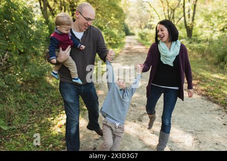 Genitori felici che fanno dondolare il bambino mentre si tengono per mano nel parco naturale Foto Stock