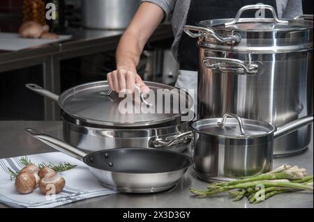 Chef al lavoro con utensili da cucina in acciaio inossidabile e prodotti freschi Foto Stock