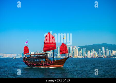 Crociera turistica in stile tradizionale in barca a vela con vele rosse attraversa il porto di Victoria da Kowloon all'isola di Hong Kong Foto Stock