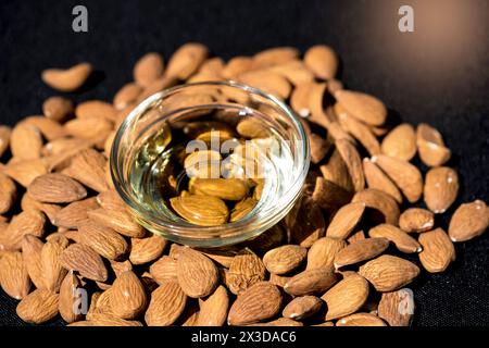 Mandorle (Prunus dulcis, Prunus amygdalus, Amygdalus communis, Amygdalus dulcis), mandorle crude con una ciotola in vetro di olio di mandorle Foto Stock