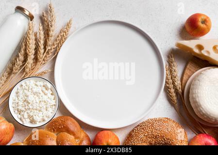 Festa ebraica religiosa Shavuot sfondo con prodotti caseari, formaggio, pane, colture di grano e piatto bianco vuoto per testo, spazio copia. Felice Shavuot Foto Stock