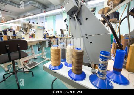 Workshop con macchine da cucire di una moderna fabbrica di scarpe, focalizzazione sulle bobine, persone sfocate Foto Stock