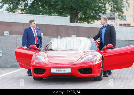 MOSCA, RUSSIA - 22 giugno 2016: Due giovani uomini d'affari (con le versioni dei modelli) che andranno a fare un giro su una supercar rossa di lusso Ferrari Foto Stock