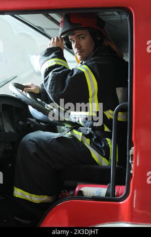 Ritratto di un pompiere che indossa i proiettili dei pompieri, seduto al volante del motore dei pompieri Foto Stock