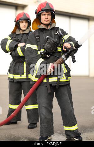 Ritratto di due pompieri eroici che tengono e regolano l'ugello e il tubo antincendio spruzzando acqua ad alta pressione Foto Stock