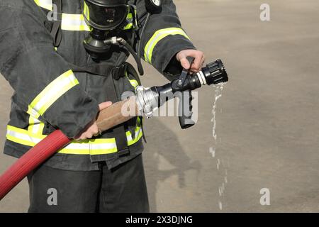 il pompiere tiene e regola l'ugello e il tubo antincendio spruzzando acqua ad alta pressione, senza getto Foto Stock