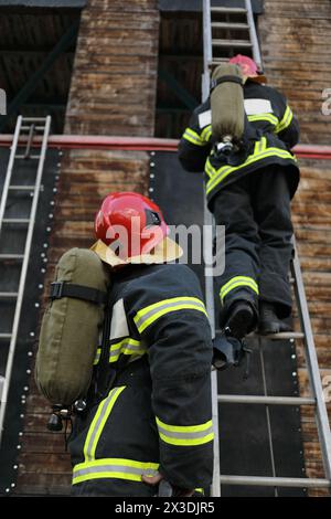 due vigili del fuoco in attrezzature e caschi sul sito di test, uno di loro sale a scala Foto Stock