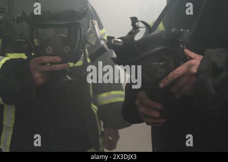 Due pompieri in un ambiente affumicato contengono maschere protettive, frammenti Foto Stock