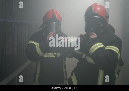 Due pompieri in tute protettive in maschere protettive in camera di fumo, ritratto a mezza altezza Foto Stock