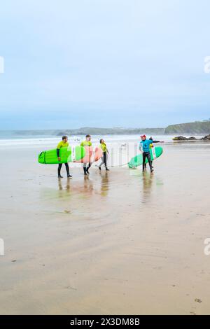 Un istruttore di surf della Escape Surf School che cammina con un gruppo di surfisti principianti sulla spiaggia di Towan a Newquay, in Cornovaglia, nel Regno Unito. Foto Stock