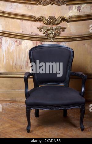 Sedia vintage nera morbida contro una parete squallida con modanature dorate Foto Stock