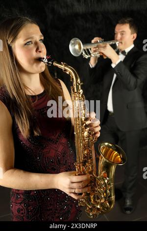 Donna che suona al sassofono di fronte a un uomo con tromba in una stanza nera Foto Stock