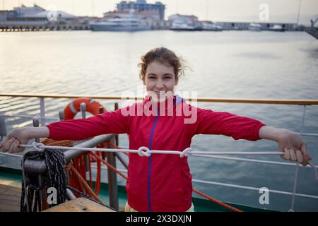 La ragazza con la giacca rossa regge la corda con tre nodi sul ponte della nave. Foto Stock