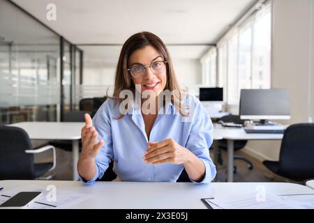 Dirigente di mezza età che parla con la webcam seduta alla scrivania. Foto Stock