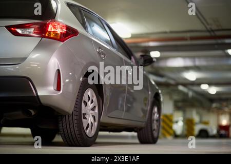 Auto argentata nel parcheggio sotterraneo, vista dal lato posteriore basso. Foto Stock