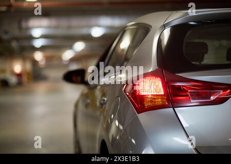 Lato conducente dell'auto argentata nel parcheggio sotterraneo, concentratevi sulle luci di posizione posteriori. Foto Stock