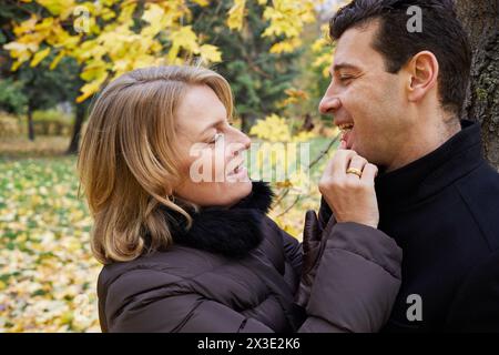 Uomo e donna sotto l'acero nel parco autunnale, guarda i suoi denti inferiori. Foto Stock