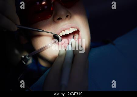 Il dentista fa la pulizia dei denti a ultrasuoni per i bambini utilizzando strumenti speciali in clinica odontoiatrica. Foto Stock