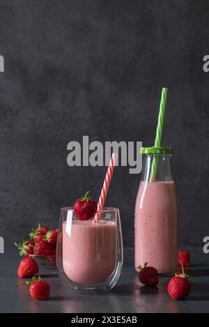 Fragola indiana lassi o frullato su sfondo grigio. Bevanda tradizionale ayurvedica sana con fragole di yogurt e cubetti di ghiaccio in bottiglia e. Foto Stock