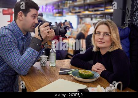 L'uomo scatta una foto di una donna seduta al tavolo in un bar. Foto Stock