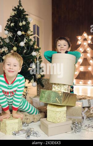 Due bambini con molti regali sono in camera con l'albero di natale, concentrati sul ragazzo giusto Foto Stock