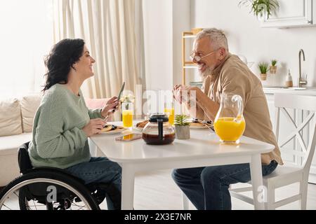 Un uomo e una donna in sedia a rotelle impegnati in una conversazione in un ambiente di cucina domestica. Foto Stock