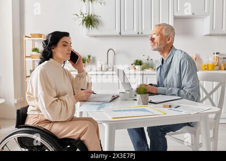 Un uomo e una donna siedono a un tavolo, concentrati sullo schermo di un notebook, impegnati in un lavoro collaborativo nella loro cucina di casa. Foto Stock