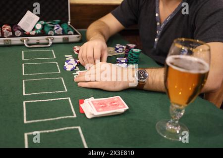 Mani maschili, patatine da casinò in caso, birra di cartone sul green table durante la partita Foto Stock