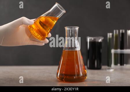 Donna che versa olio greggio giallo nel matraccio sul tavolo grigio, primo piano Foto Stock