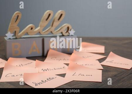 Cubi con la frase Hello Baby e adesivi di carta con nomi diversi su un tavolo di legno, primo piano. Scegliere il nome del bambino Foto Stock