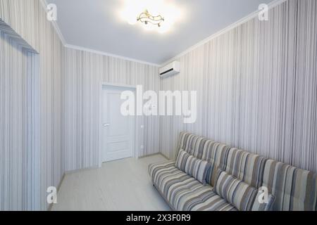 Camere vuote, semplici e accoglienti, con pareti a righe e divano a righe, aria condizionata Foto Stock