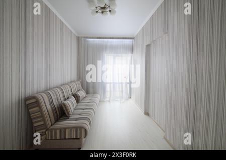 Camera vuota, semplice e accogliente, con porta del balcone, pareti a righe e divano a righe Foto Stock