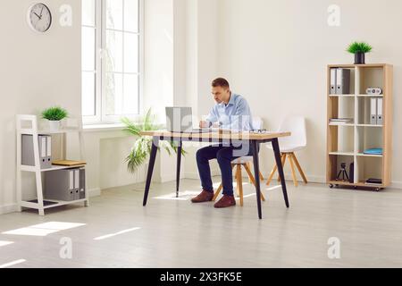 Giovane e attraente uomo d'affari che lavora sul posto di lavoro con un notebook in un ufficio moderno. Foto Stock