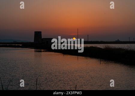 Antico mulino a vento nelle Saline di Trapani e Paceco al tramonto in Sicilia. Foto Stock