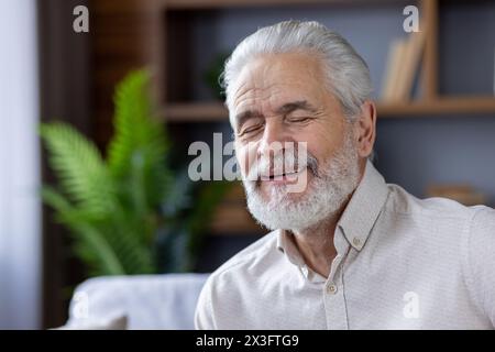 Foto ravvicinata di un vecchio uomo dai capelli grigi sorridente a casa, che riposa con gli occhi chiusi e che sogna con attenzione. Foto Stock