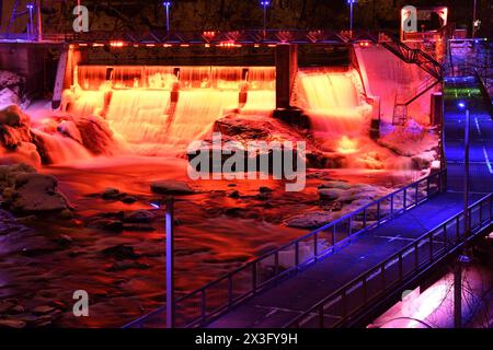 Sherbrooke Magog River in centro di notte. Diga di potenza illuminata di colore rosso con penstock e passerella in acciaio. Ambientazione invernale urbana di una splendida illuminazione Foto Stock